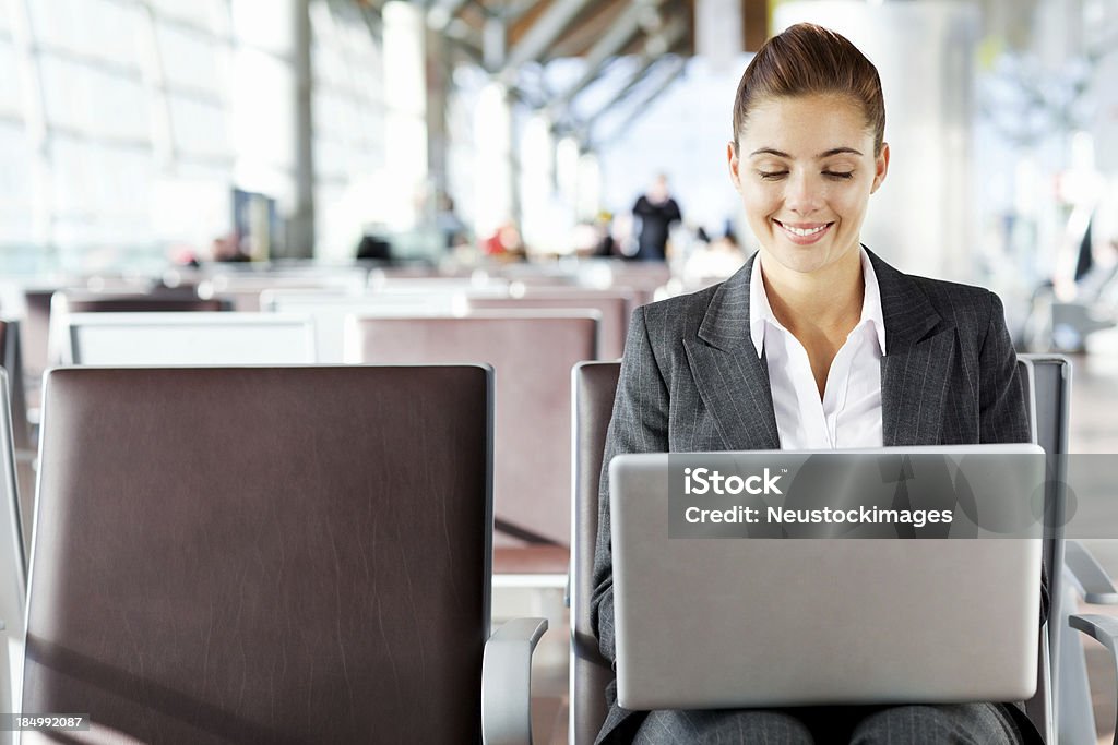 Businesswoman Working On Laptop At Airport Smiling young business woman working on a laptop in departure lounge. Horizontal shot. Adult Stock Photo