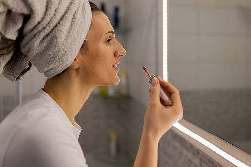 Elegant young woman putting on her favorite lipstick in bathroom