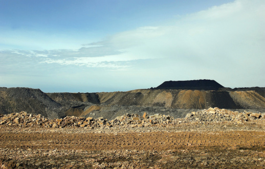 Dirt road for heavy equipment at a Pennsylvania coal strip mine with excavated rock and coal piles in the background.