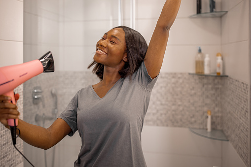 African American Woman Blow Drying Her Hair in Bathroom