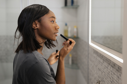 Young African American Woman Applies Vibrant Lipstick in Bathroom