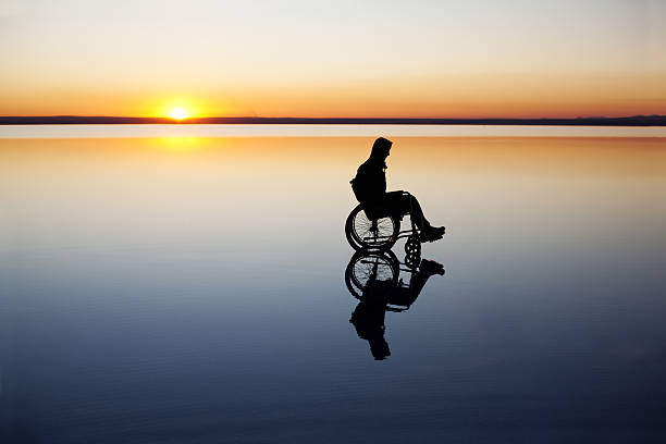 Silhouette of a disabled man in a wheelchair at sunset stock photo