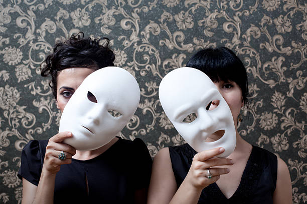 Two women peeking behind mask on wallpaper background stock photo