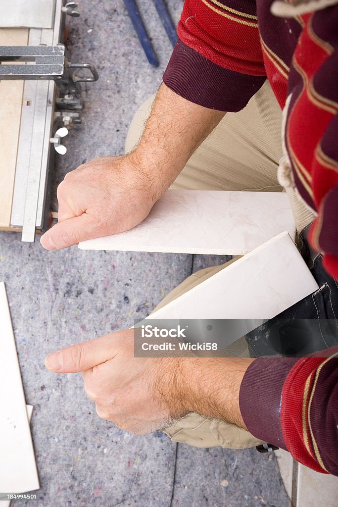 Tile Breaking "Home improvement background, over shoulder view at tilers work, a tile setter has used a manual bar cutter to score and cut a ceramic tile. After cutting the tile he applied equal pressure on both edges of the tile at the same time using knee as support. The tile broke along the score mark and left a clean cut." Adult Stock Photo