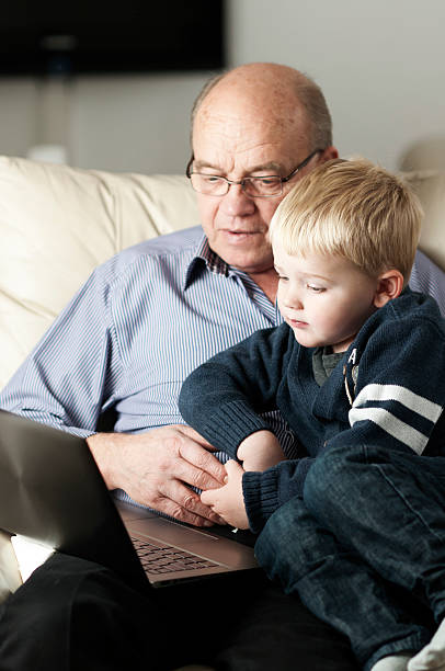 grand-père et le petit-fils ensemble sur ordinateur portable - generation gap multi generation family vertical holding hands photos et images de collection