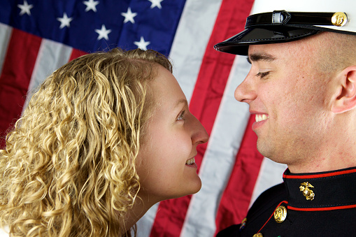 Young Marine with wife, American flag in the background.