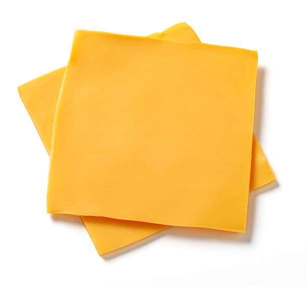 American Cheese Slices Two slices of processed American cheese on white background with natural shadow. cheddar cheese stock pictures, royalty-free photos & images