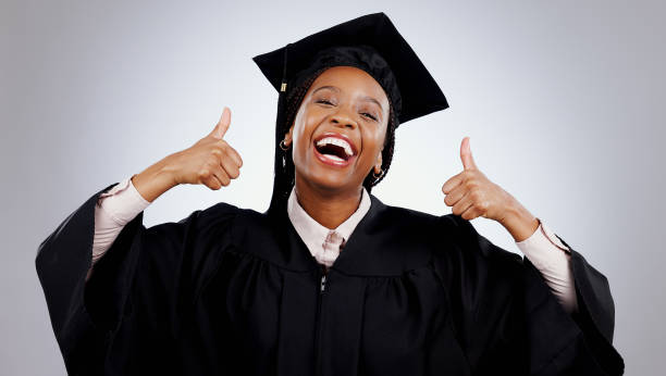 istock Graduation, woman and student thumbs up for study success, celebration and education, learning or college in studio. Portrait of excited African graduate with yes and like emoji on a white background 1849971096