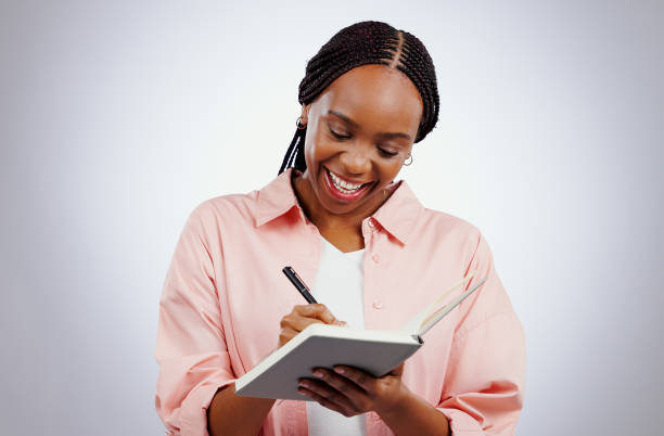 Happy woman, notebook and writing ideas, planning or creative solution for studying, college or education goals in studio. African student with book reminder or notes for learning on white background