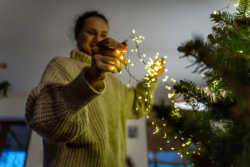 Young woman decorating a Christmas tree with Christmas lights and garland.