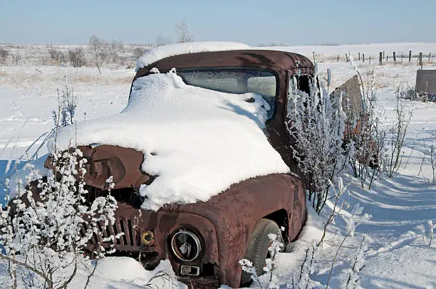 A 40's pickup abandoned in a field and covered with snow.