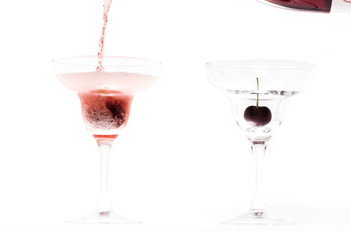 Red cherry and champagne being poured in martini glasses on isolated white background.