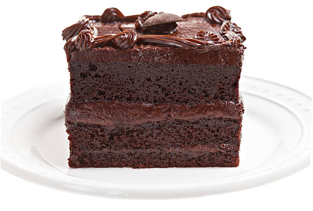 A close up of a square slice of a multilayered chocolate fudge cake on a white round plate. Isolated on white.