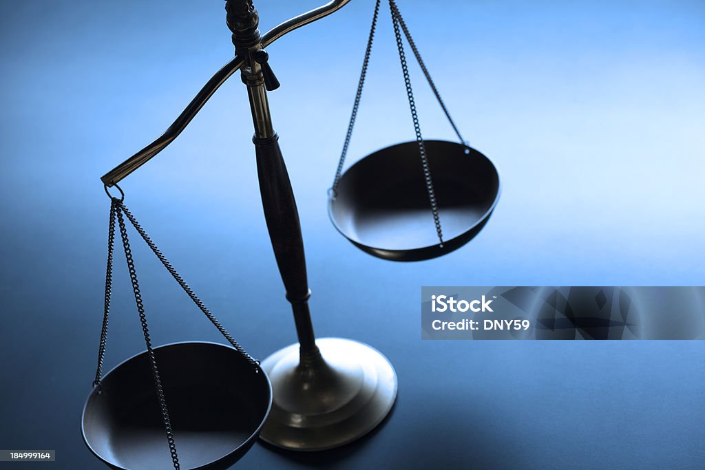 Lone justice scale on simple blue background A justice scale on a simple blue background.  The scale is partially silhouetted as a strong backlight obscures some of the finer details.  Scale is place on left hand side of image leaving ample negative space for copy. Image can be flipped horizontal to accommodate alternative composition needs. Weight Scale Stock Photo