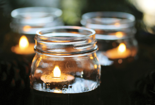 Tea light candles float in canning jars filled with water.  The jars are set among pine boughs and pine cones.