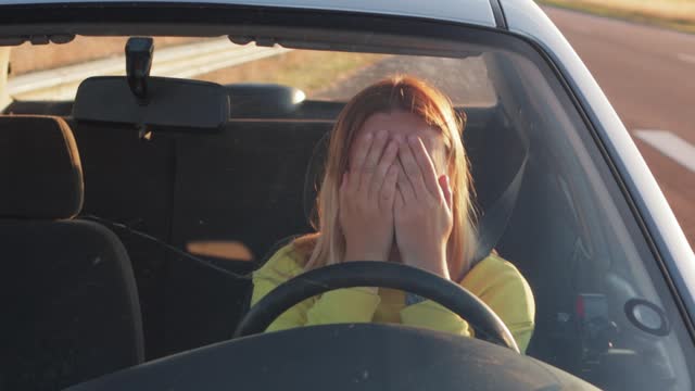 girl in a yellow jacket sits behind the wheel of a car sad, holds on to the steering wheel and screams strongly does not know what to do the car broke down on the road. High quality 4k footage