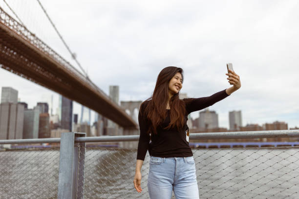 istock Chinese girl exploring NYC, taking selfie under the Brooklyn Bridge 1850032856