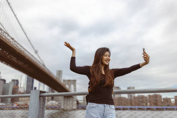 istock Chinese girl exploring NYC, taking selfie under the Brooklyn Bridge 1850034817