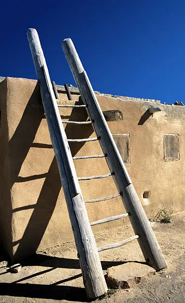 "A wooden ladder leans against the wall of an adobe home at the Acoma Pueblo, New Mexico, USA.  Acoma Pueblo is the oldest inhabited settlement in the United States. The ancient pueblo, known as the Sky City, is spectacularly situated like a medieval fortress atop its 600-foot-high rock, halfway between Gallup and Albuquerque in New Mexico USA"