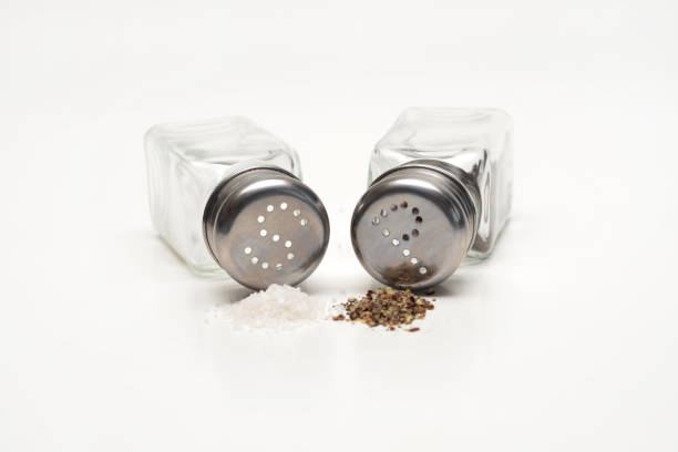 Close up of salt and pepper shakers with small heaps of salt and pepper in front on a white background.