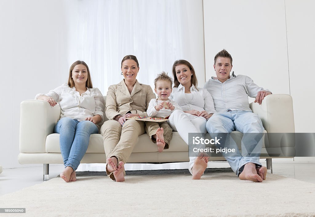 family on sofa "portrait of a smiling teenage girl, two young adult women, a baby boy and an young adult man sitting on a sofa in the living room looking at the camera" 20-24 Years Stock Photo