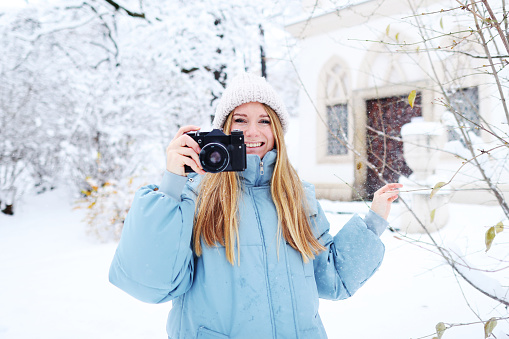 Blond smiling girl photographed on an old vintage camera in winter forest