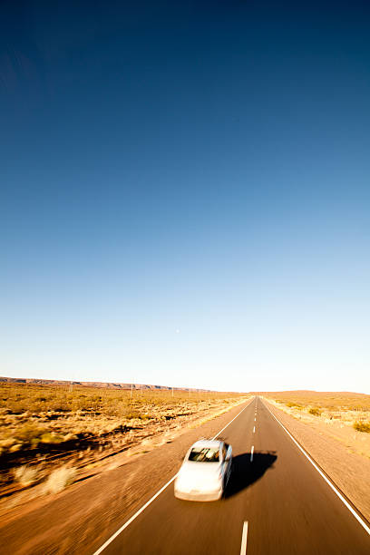 White car speeding down a long desert road (route 20) in the Patagonia region of Argentina. Motion blur on car.