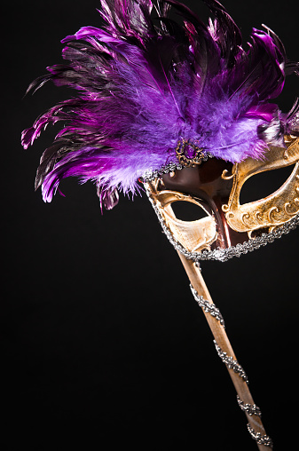 Ball mask. Golden masquerade carnival mask with purple feathers isolated on black background.