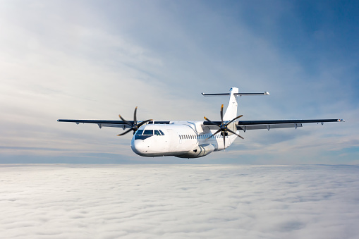 White passenger turboprop aircraft flies in the air above the clouds