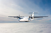 White passenger turboprop aircraft flies in the air above the clouds