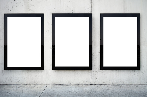 Blank billboards on wall. Wall is made of concrete and gray coloured. There are three billboards standing side by side and oriented vertically. Edges of billboards are black. Billboards are empty so you can write or add something on them. - Clipping path of billboards included.