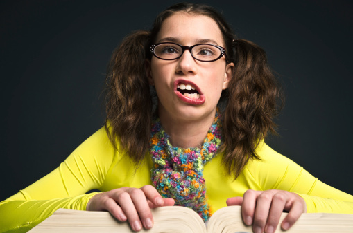 A nerdy girl looks up from her book making a face.