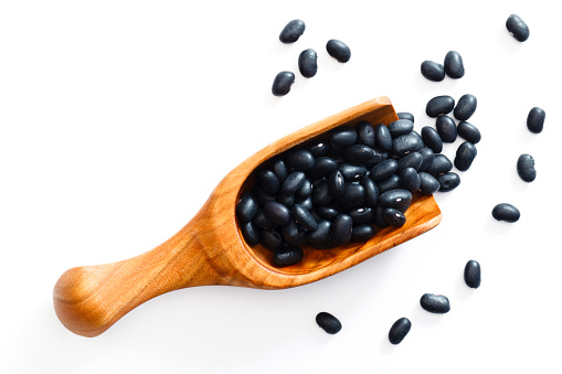 Black beans spill from a wooden scoop