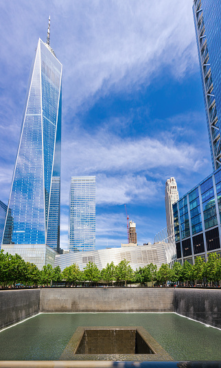 World Trade Center Towers, Pool with Waterfall of the 9/11 Memorial and Oculus Transportation Hub with Blue Sky in Background. The Pool is where the Footprints of the Twin Towers were and is Free for Public Viewing, New York City, NY, USA. Vertical Stitched Panoramic image. Canon EOS 6D (full frame sensor) DSLR and Canon EF 24-105mm F/4L IS lens.