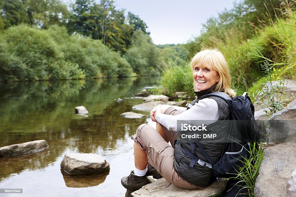 Muito sênior mulher sentada em rochas do rio - Foto de stock de Acampar royalty-free