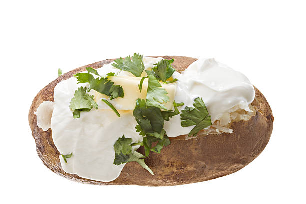 Baked Potato "A high angle close up of a baked potato with sour cream, melting butter and garnished with some coarsely chopped fresh cilantro leaves." baked potato sour cream stock pictures, royalty-free photos & images