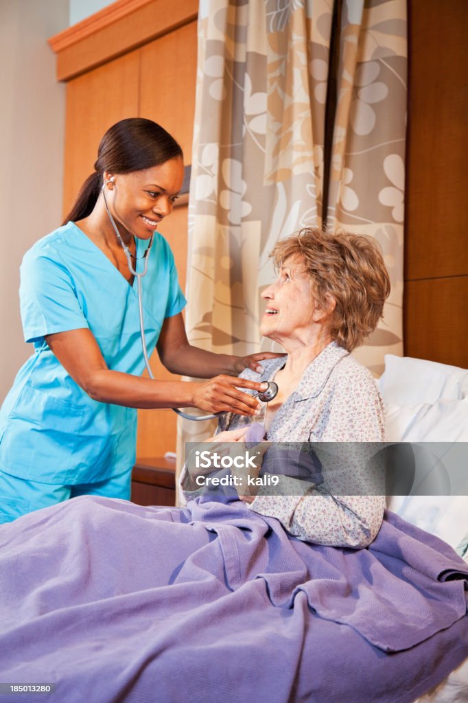 Nurse examining senior woman in hospital room African American nurse (40s) using stethoscope of listen to heart of senior woman (80s) in hospital room. 40-49 Years Stock Photo