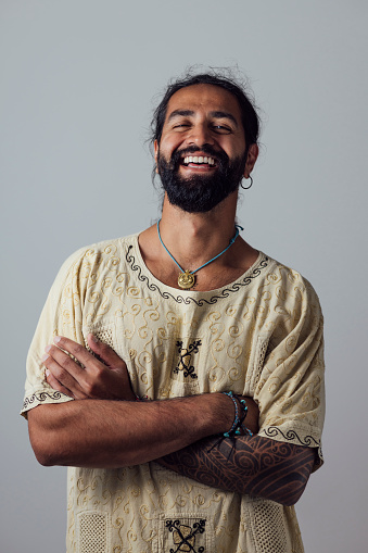 Portrait of a mid-adult Asian man standing in front of a grey studio background. He is posing with his arms folded, laughing and looking at the camera.