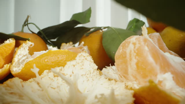 A man takes segments of a peeled mandarin from the table, among a large pile of fruits. Dolly slider extreme close-up.