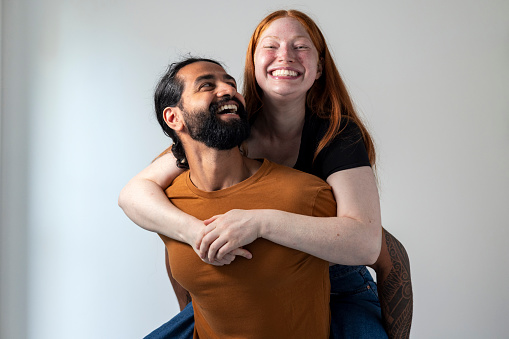 Front view, waist up, shot of two friends in front of a grey studio background. The young female is looking at the camera and smiling while the male adult looks at her and smiles.