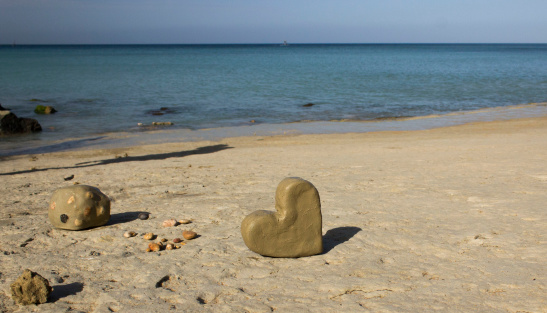 Hart shaped pebble on sand on a beach.