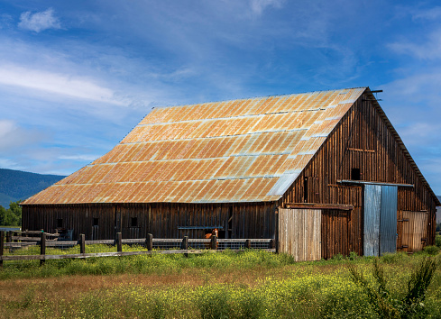 Large barn with one horse in the corral.