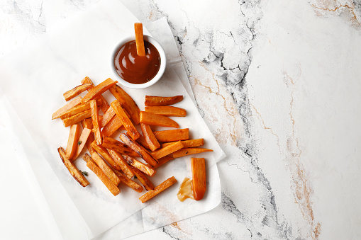 Fried sweet fries with thyme, spices, saucerm, lemon, on a marble background