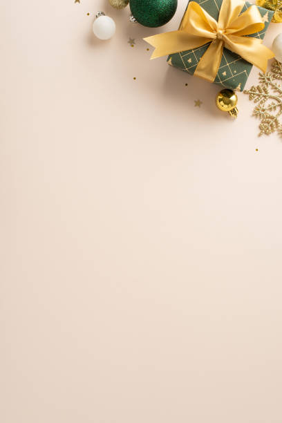 istock Luxurious New Year concept with touch of creativity. Top-view vertical image showcases ribbon-decorated gift, lavish baubles, snowflake detail, glistening sequins against light backdrop, space for ads 1850291717