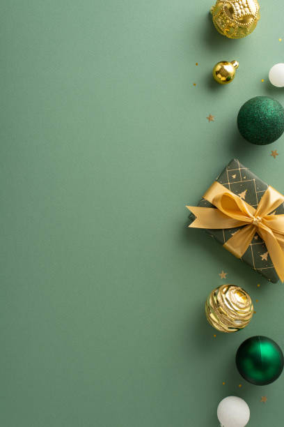 istock Contemporary festive mood. Top-view vertical shot featuring stylishly wrapped gift, extravagant ornaments, shimmering gold sequins on green surfaceâample space for personalized wishes or advertisement 1850292274