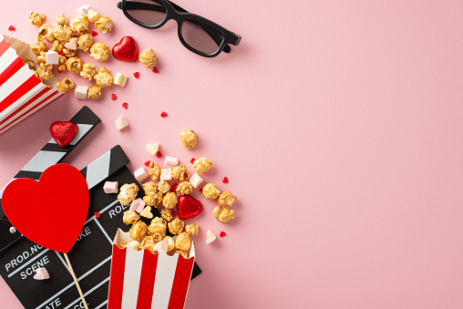 Valentine's movie magic. Top view shot showcasing clapper, 3D specs, popcorn boxes, heart-shaped ornaments, candies, marshmallows, sprinkles on lovely pastel pink surface, creating dreamy atmosphere