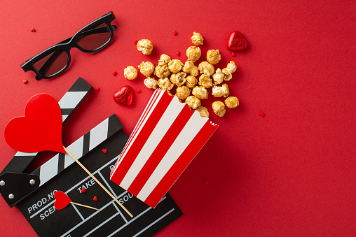 Valentine's Cinema Affair: top view of clapperboard, 3D glasses, popcorn cascading from box, sweet chocolate treats, heart-shaped ornaments on redâ cinematic celebration for premiere of romantic film