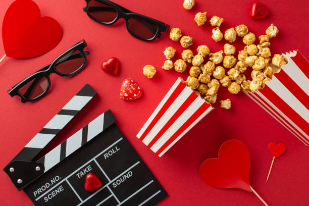 istock Premiere Passion: Top-view image of clapper, 3D glasses, popcorn scattered from box, delectable chocolates, and heart-adorned sticks on striking red backgroundâcrafted for premiere of a romantic film 1850293838
