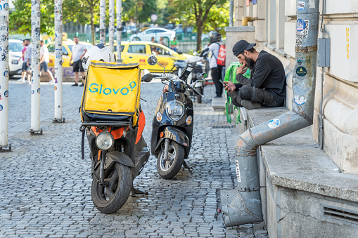 Bucharest, Romania - August 17 2023: Glovo food delivery courier checking his phone for orders in the old town center of Bucharest.