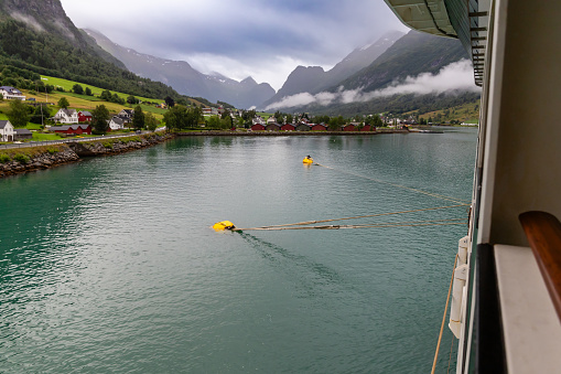 Olden, Norway-18. July 2023: Cruise view of Olden. A view from the deck of a cruise ship of Olden's calm water front and mist-shrouded mountains, copy space.